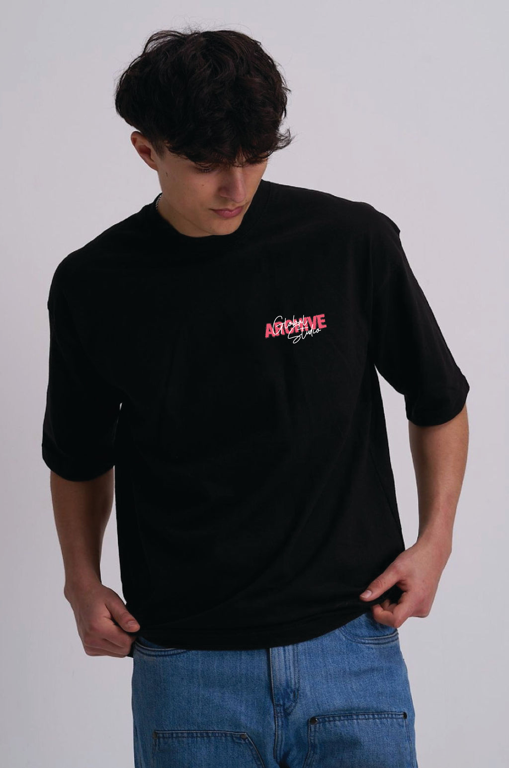A man wearing a black short-sleeve t-shirt with a pink and white 'Archive' graphic on the left chest, paired with blue jeans, photographed against a light grey studio background.