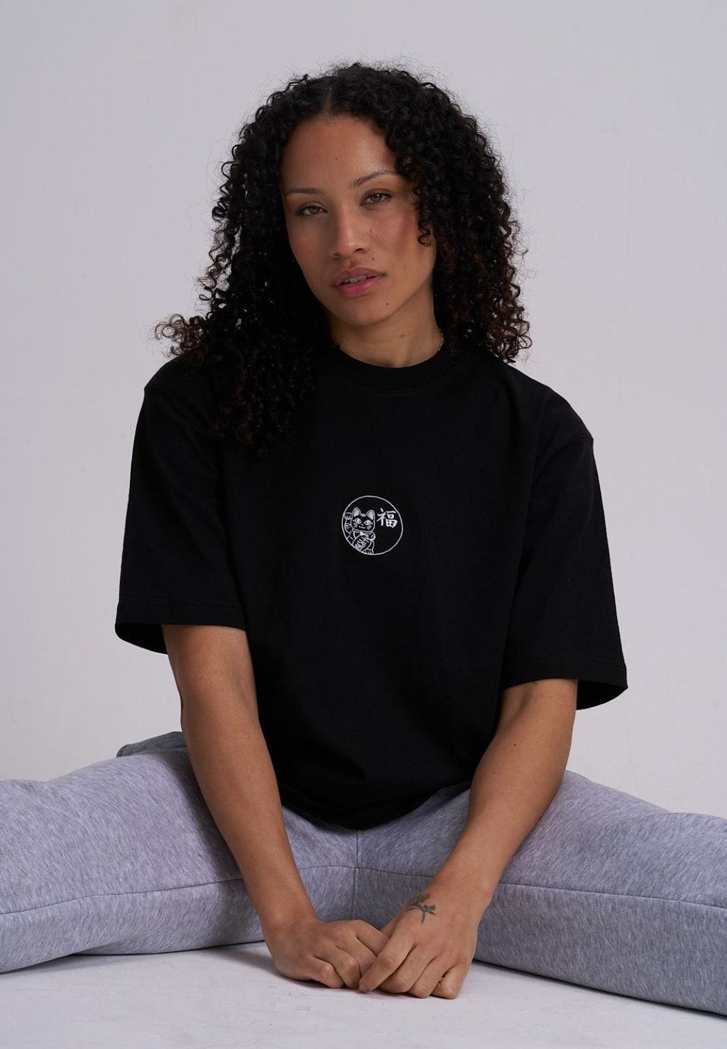 Female wearing a black tee with a lucky cat embroidery in white
