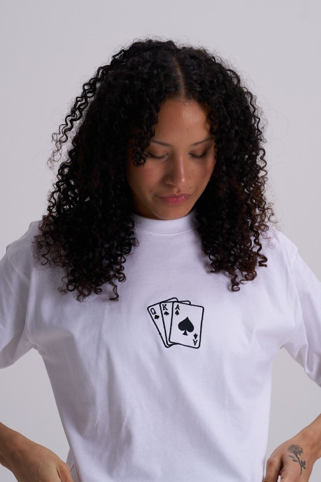 Woman wearing a white t-shirt with a black embroidered deck of cards design on a plain background