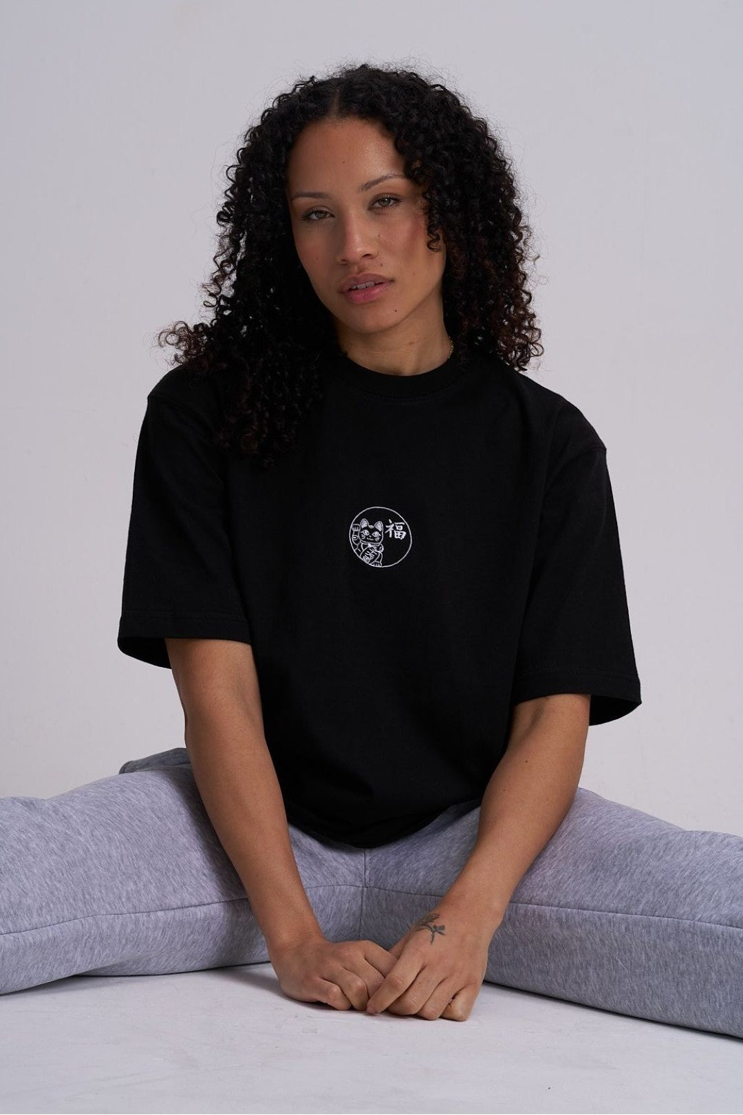 Woman wearing a black t-shirt with a logo, sitting on the floor