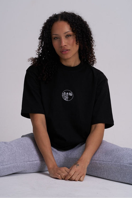 Woman wearing a black t-shirt with a logo, sitting on the floor