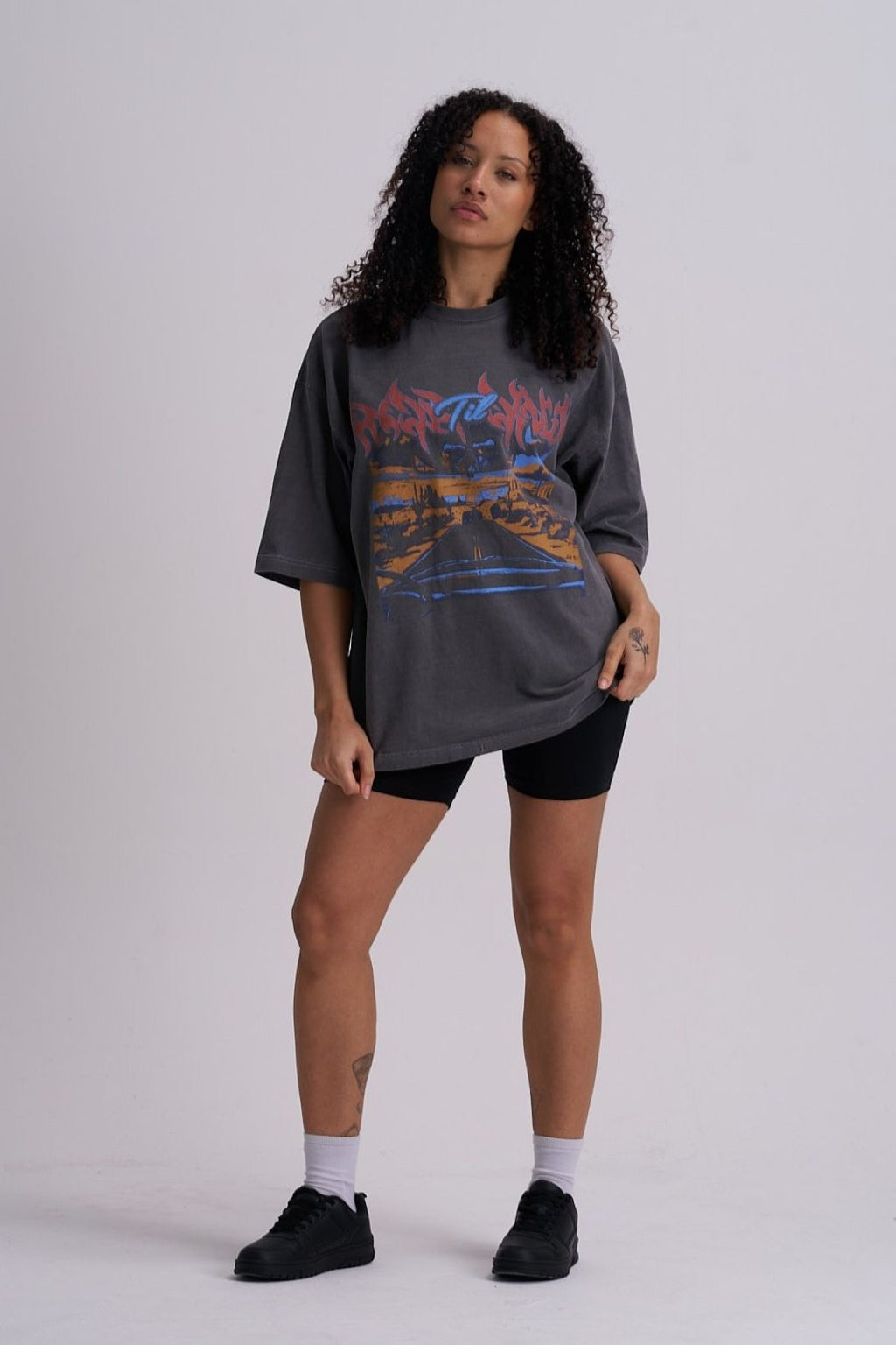Woman wearing a grey oversized t-shirt with colourful highway graphics on a plain background