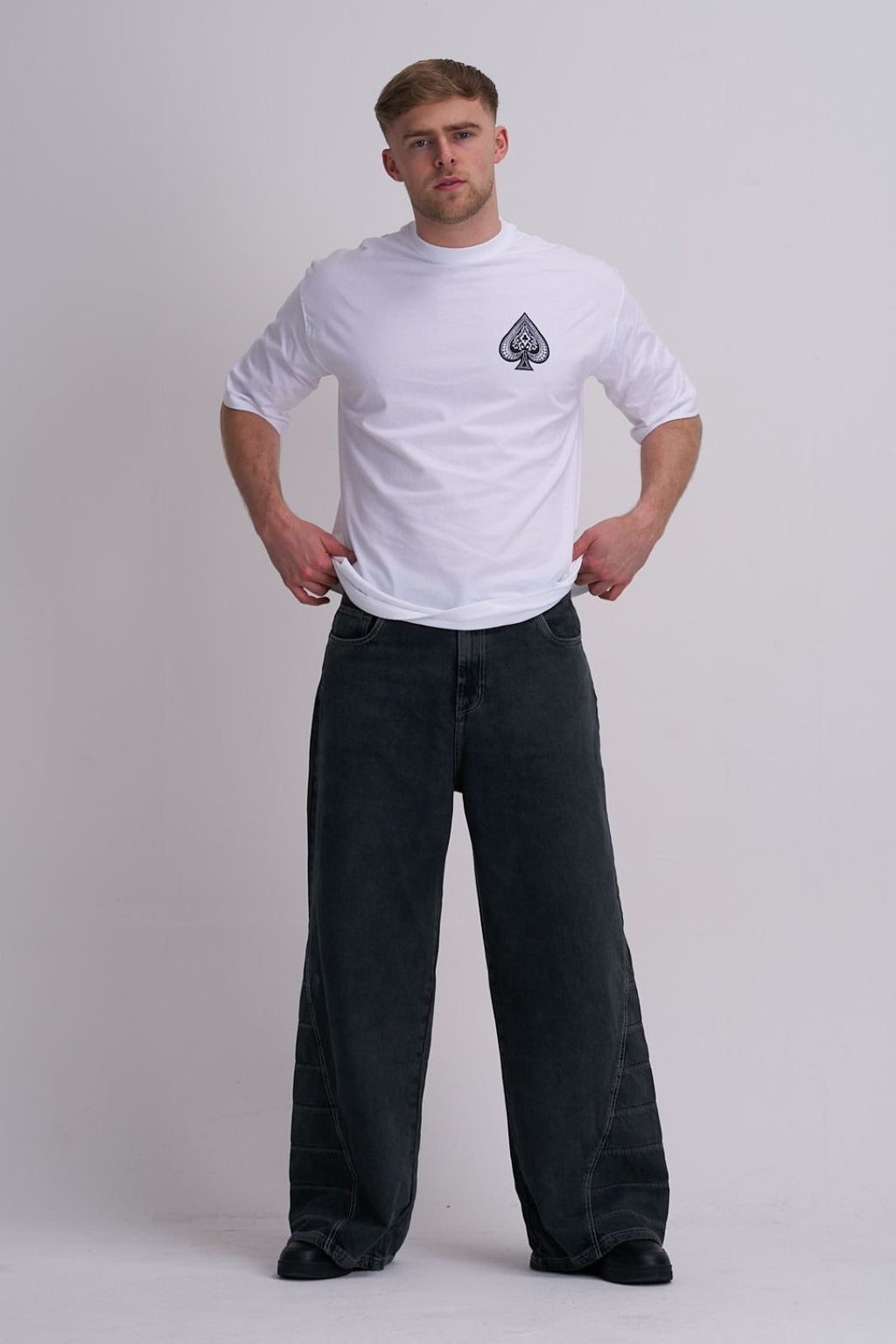 Man wearing a white t-shirt with a logo and black pants on a plain background