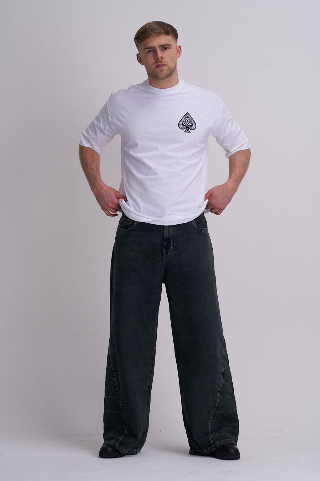 Man wearing a white t-shirt with a logo and black pants on a plain background