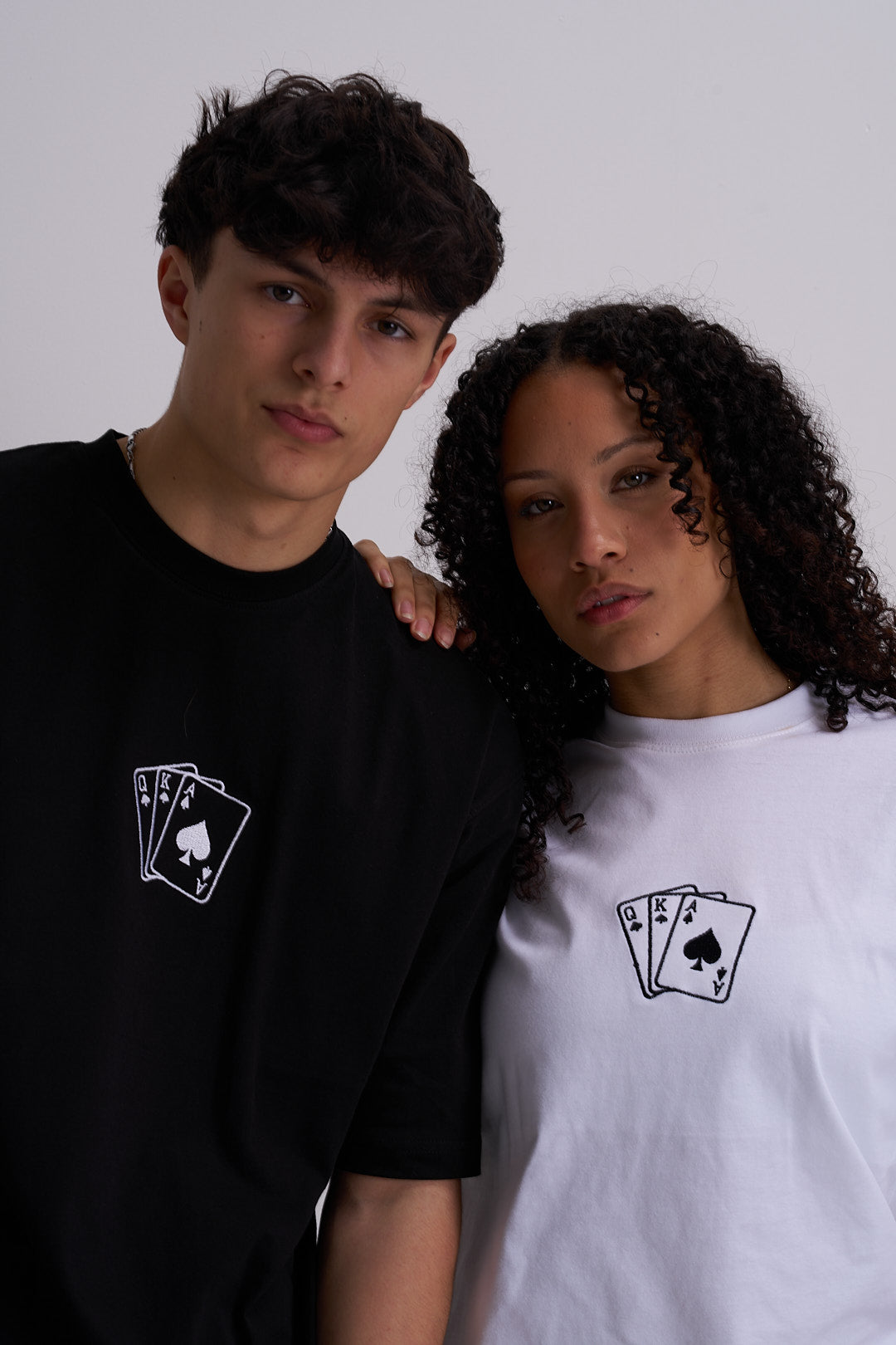 Two people wearing t-shirts with playing card design on a plain background