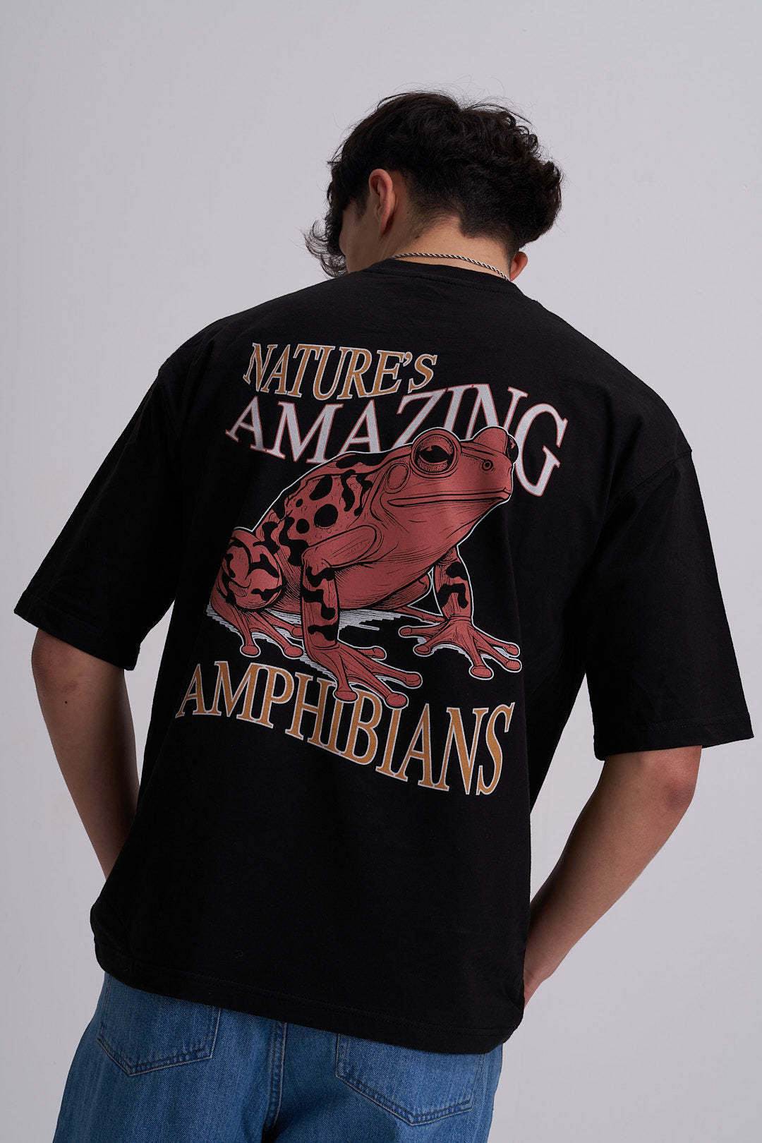 Male wearing a black t-shirt with frog graphic and amazing amphibians text on the back