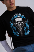 A man wearing a black long-sleeve t-shirt with a graphic print of a skull wearing a crown of blue flames, layered over a white long-sleeve shirt and blue jeans.