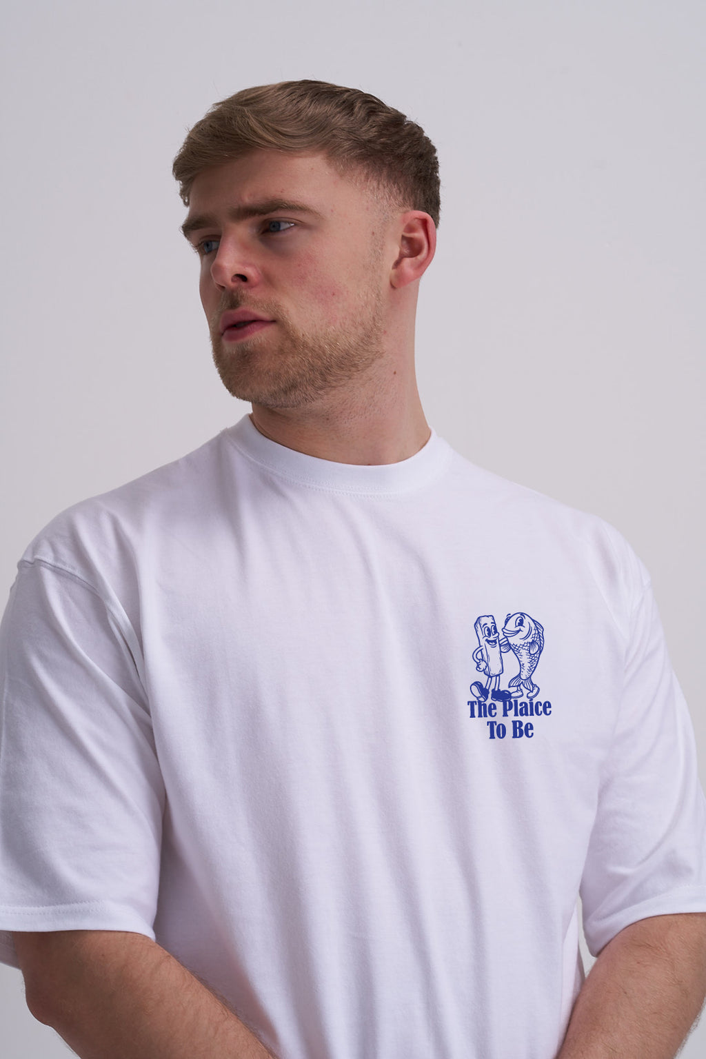 Man wearing a white t-shirt with a blue fish and chips graphic and text on a plain background