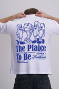 Male wearing a white t-shirt with blue graphics and The plaice to be text on the back.