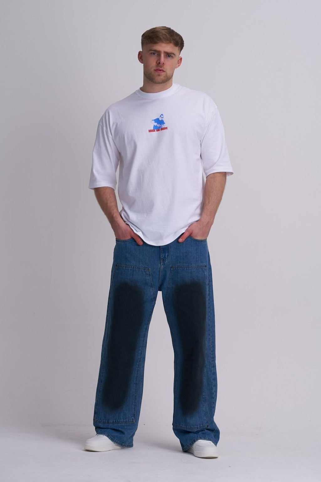 Man wearing a white t-shirt with a small pizza graphic and blue jeans on a plain background