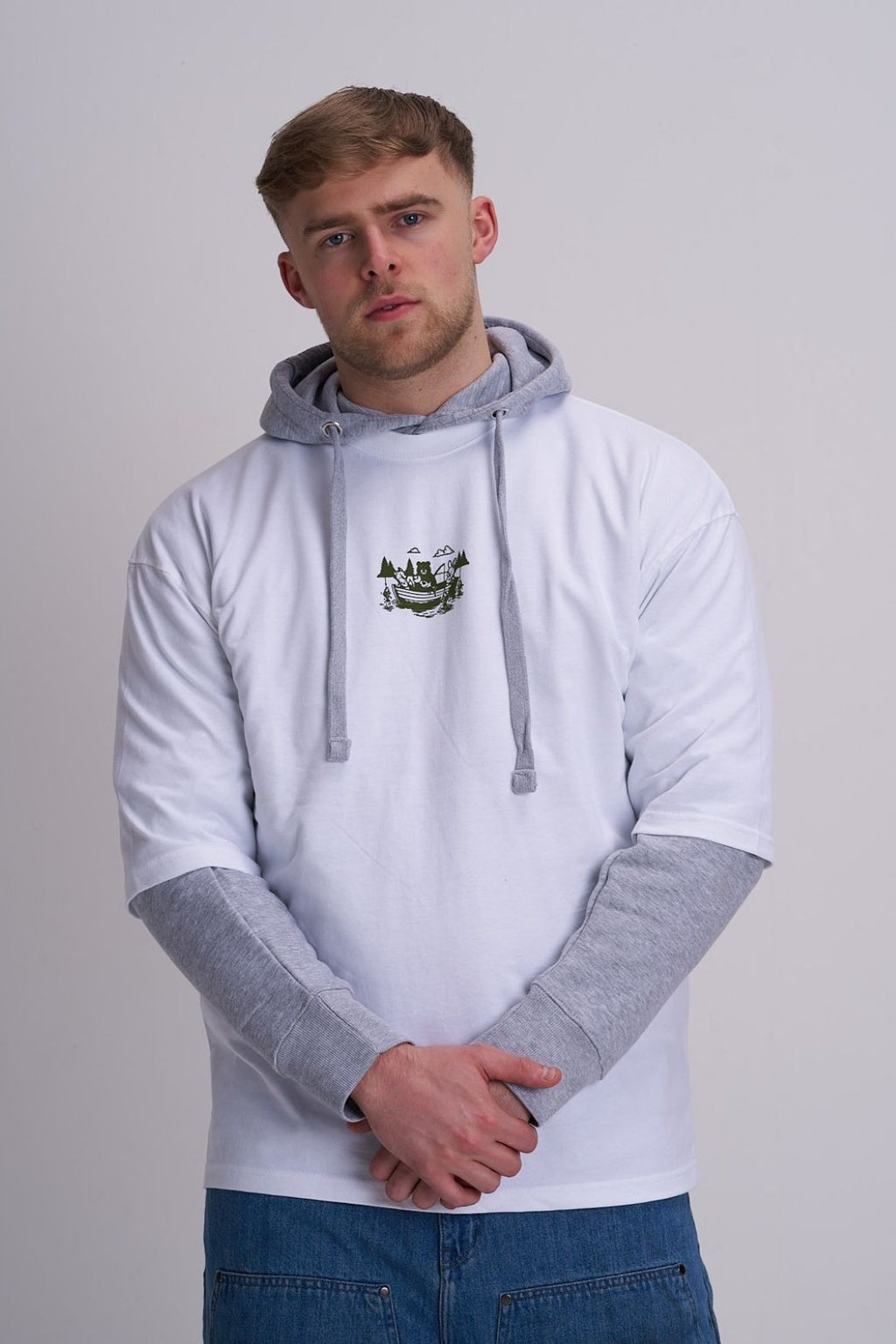 Man wearing a light grey hoodie with a t-shirt on top that has a logo of a fishing boat on a plain background