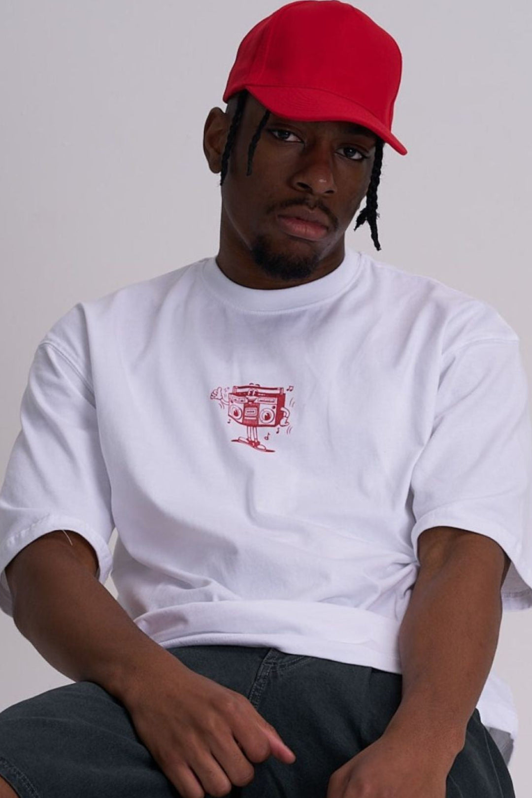 Person wearing a white t-shirt with a red retro music logo and a red cap on a plain background
