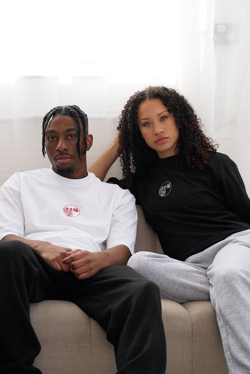 Male and female sitting on a couch wearing matching t shirts with lucky cat embroideries