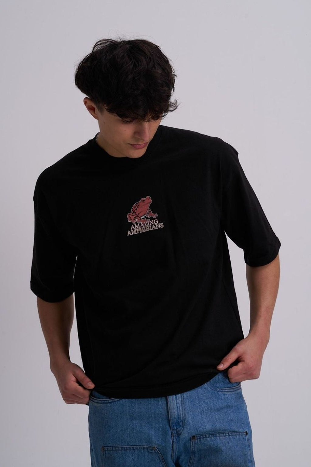 Male wearing a black t-shirt with a red frog logo on a plain background