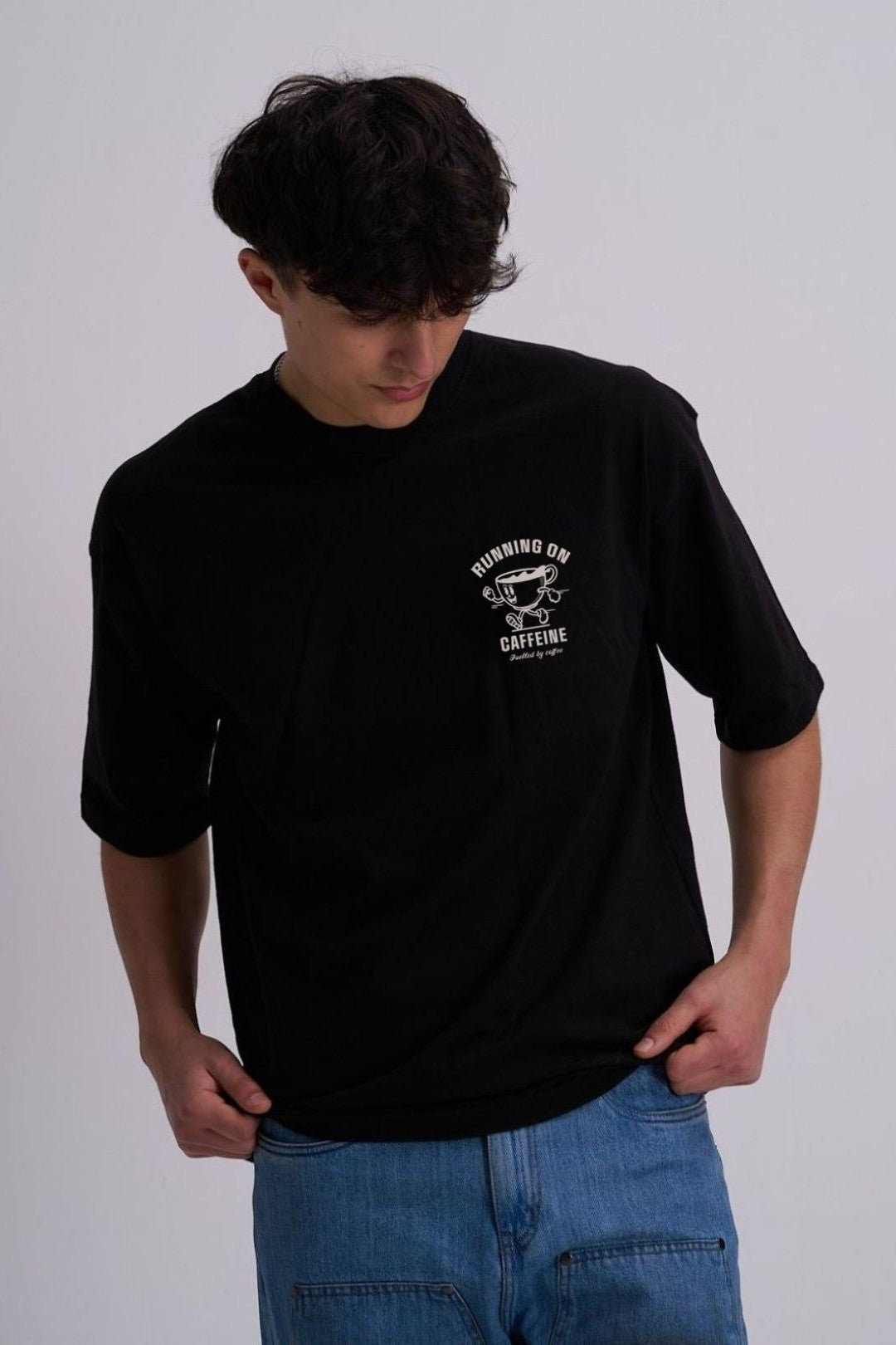 Person wearing a black t-shirt with a cartoon coffee cup logo on a plain background