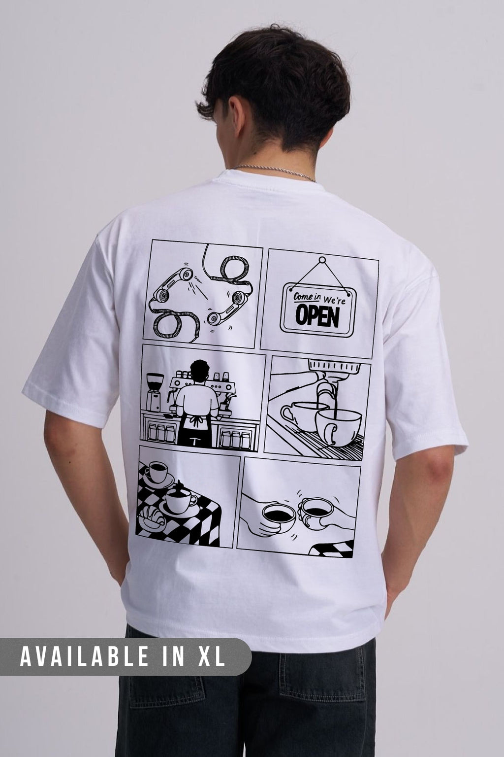 A man viewed from behind wearing a white short-sleeve T-shirt with a large black comic-style coffee graphic print on the back, paired with dark jeans against a light grey studio background. 