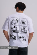 A man viewed from behind wearing a white short-sleeve T-shirt with a large black comic-style coffee graphic print on the back, paired with dark jeans against a light grey studio background. 