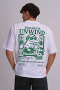 A man viewed from behind wearing a white t-shirt with a large green graphic print on the back. The graphic features a crocodile DJ with headphones, speakers, and vinyl records, with the text 'Rewind & UNWIND' and 'THE PERFECT BLEND FOR YOUR SOUL'.