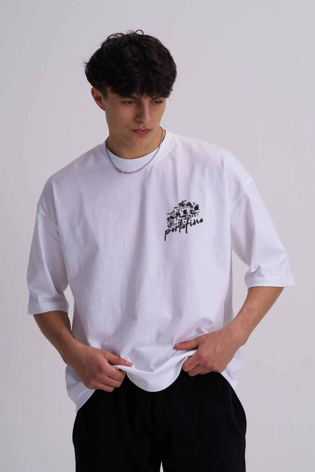 Person wearing a white t-shirt with a coastal line drawing on a plain background