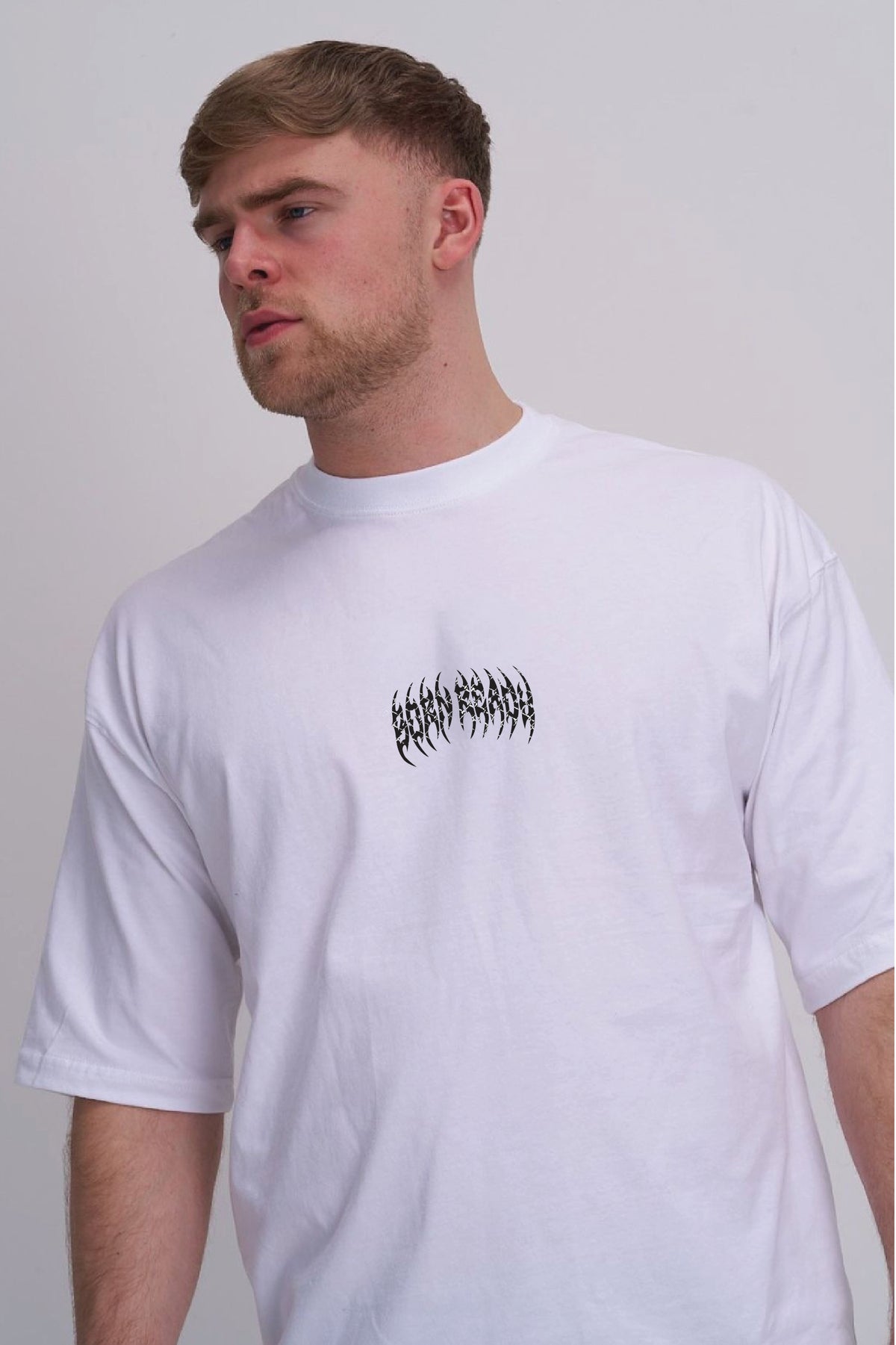 A man wearing a white crew neck t-shirt with a black stylized 'born ready' text graphic on the chest, photographed against a neutral light grey background.