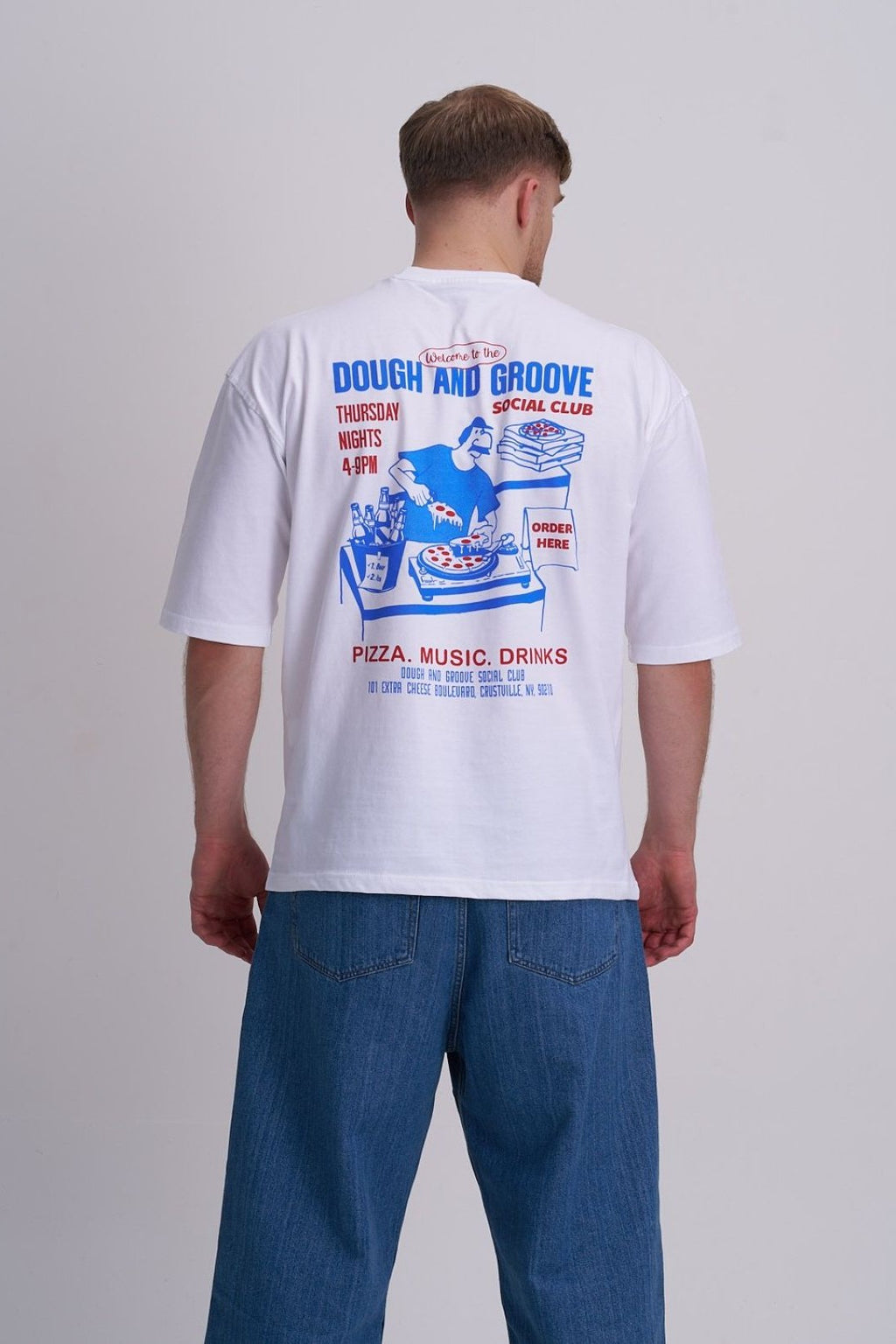 Man wearing a white t-shirt with a colourful pizza and music graphic on the back against a plain background