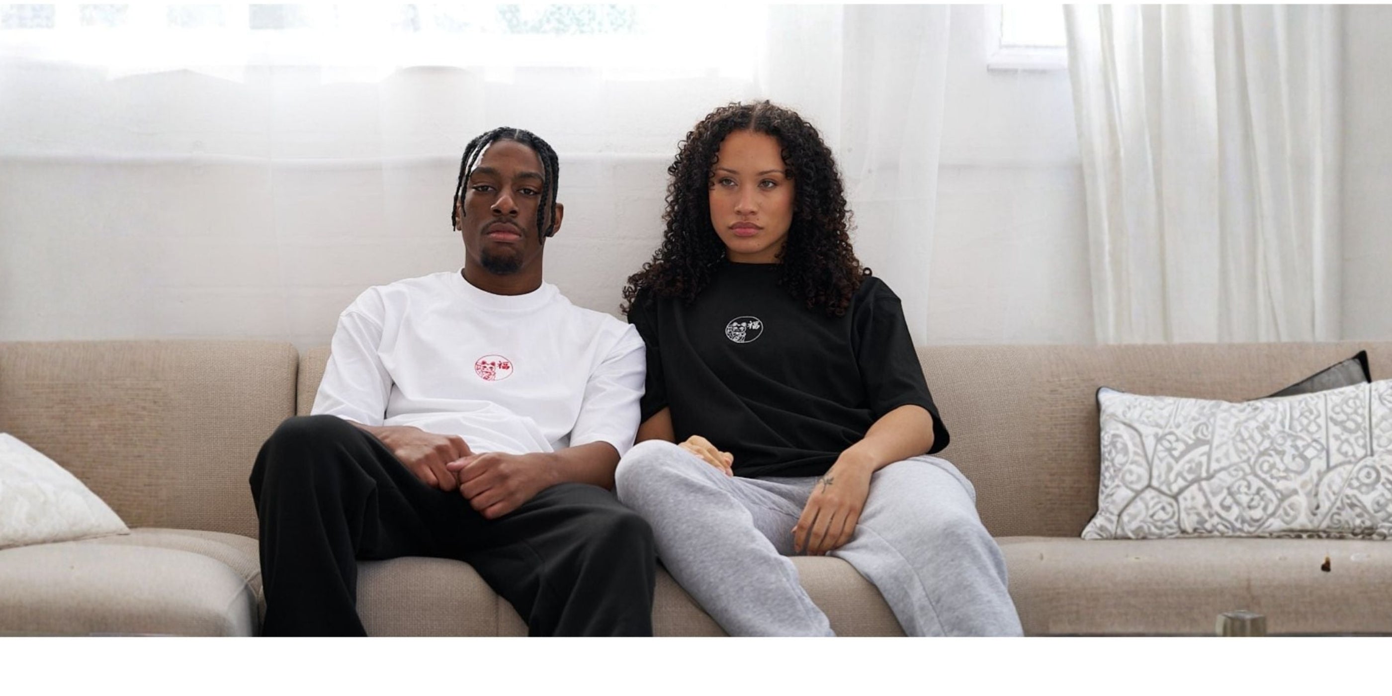 Two people sitting on a couch in a bright living room. wearing lucky cat embroidered t shirts