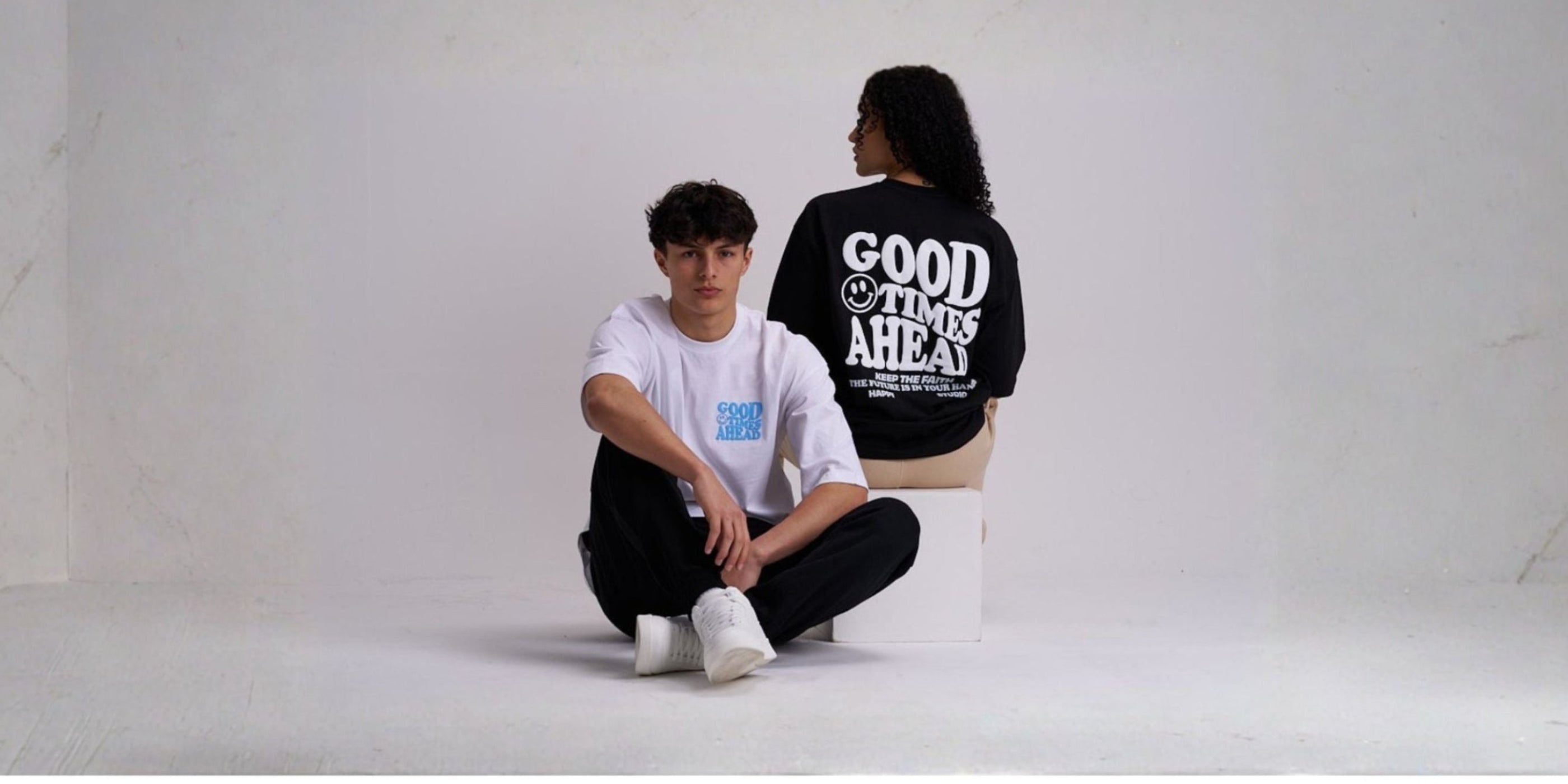Man and woman sitting on a white floor with "good times ahead" text on their shirts.