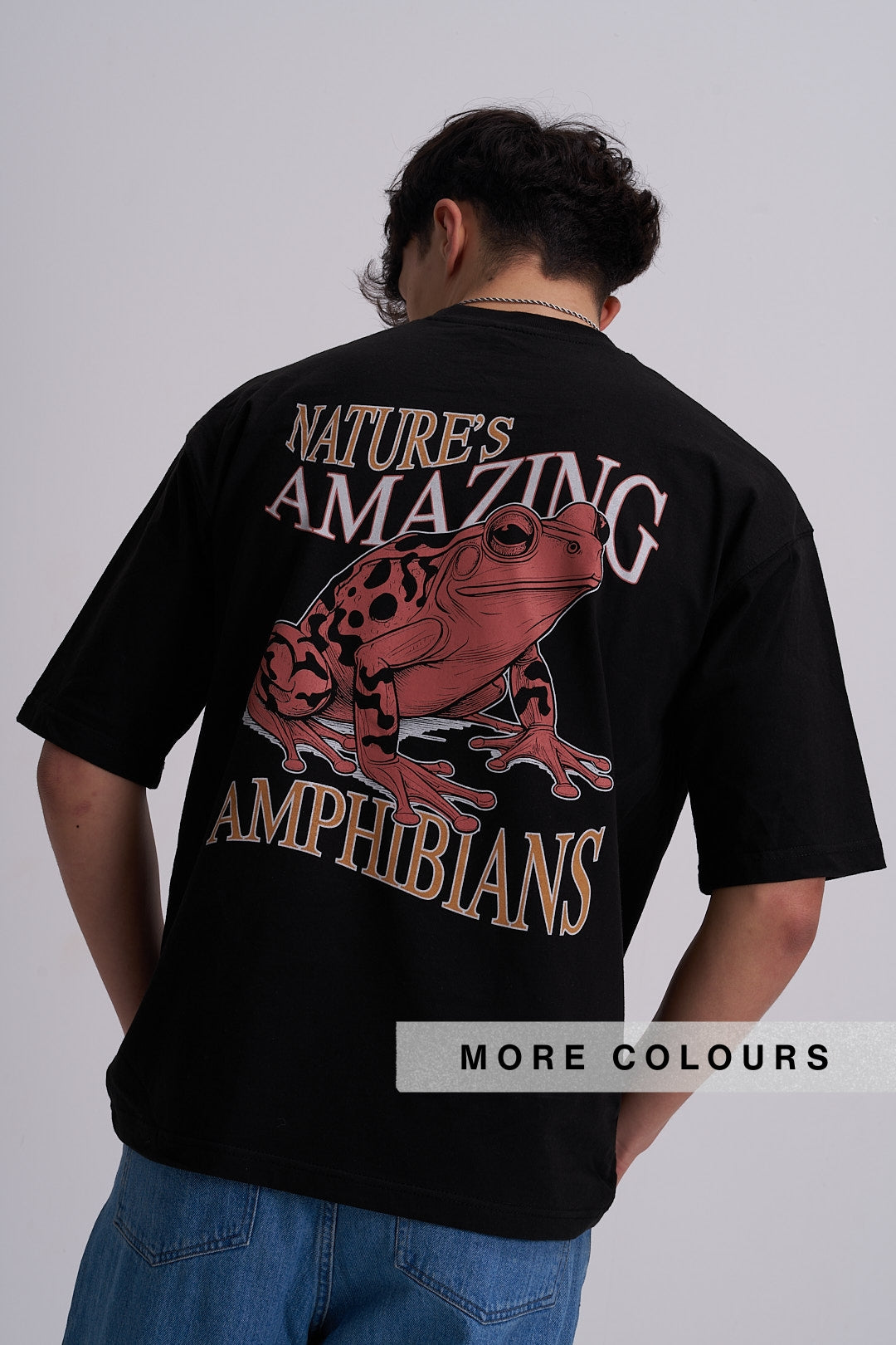 A man viewed from behind wearing a black t-shirt with a large graphic print of a red and black spotted frog and the text 'NATURE'S AMAZING AMPHIBIANS'.