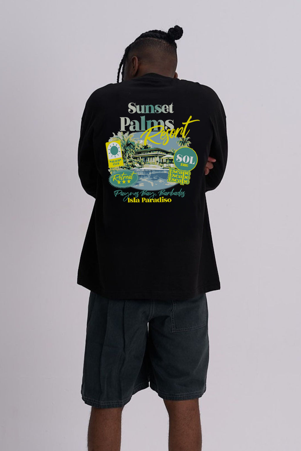A man viewed from behind wearing a black short-sleeve t-shirt with a large colourful graphic print on the back, paired with dark grey shorts, against a light grey studio background.