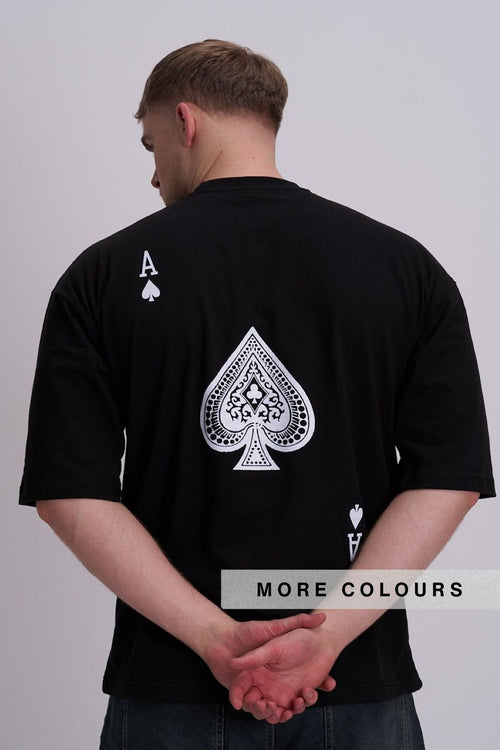 A man viewed from behind wearing a black t-shirt with a large white Ace of Spades graphic on the back, set against a plain light grey background.