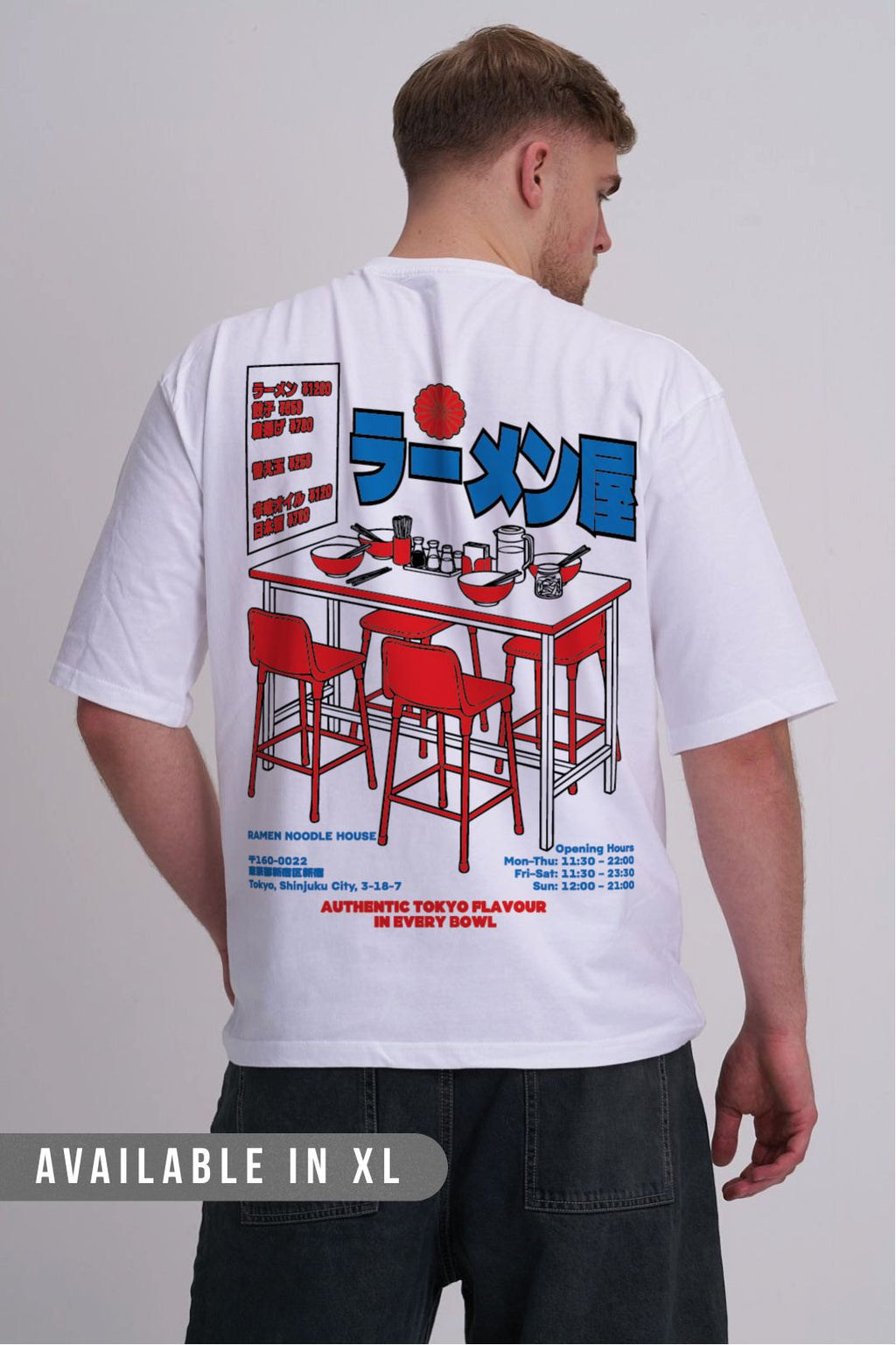 A man viewed from behind wearing a white graphic t-shirt with a large red and blue ramen restaurant illustration on the back, paired with dark jeans against a light grey studio background.