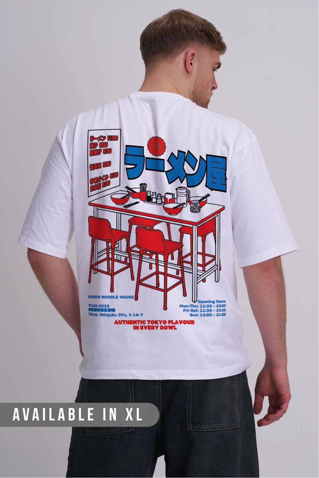 A man viewed from behind wearing a white graphic t-shirt with a large red and blue ramen restaurant illustration on the back, paired with dark jeans against a light grey studio background.