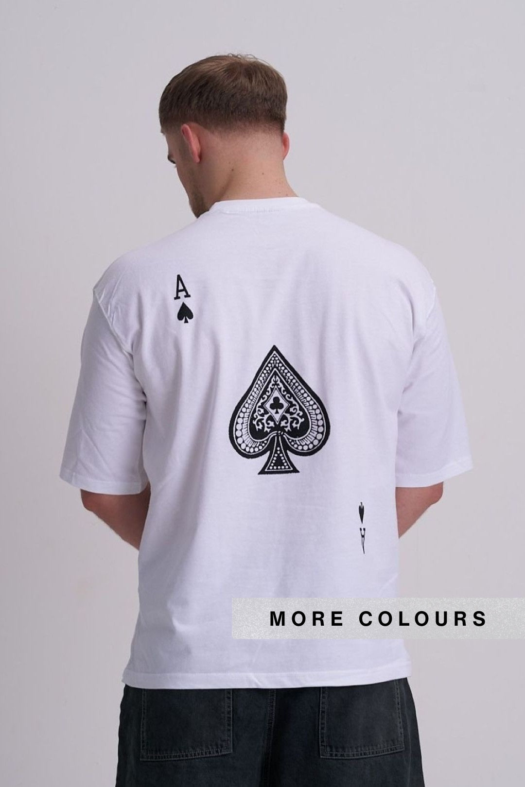 A man viewed from behind wearing a white t-shirt with a large black spade graphic on the back, featuring an Ace of Spades symbol and a small black spade icon. 