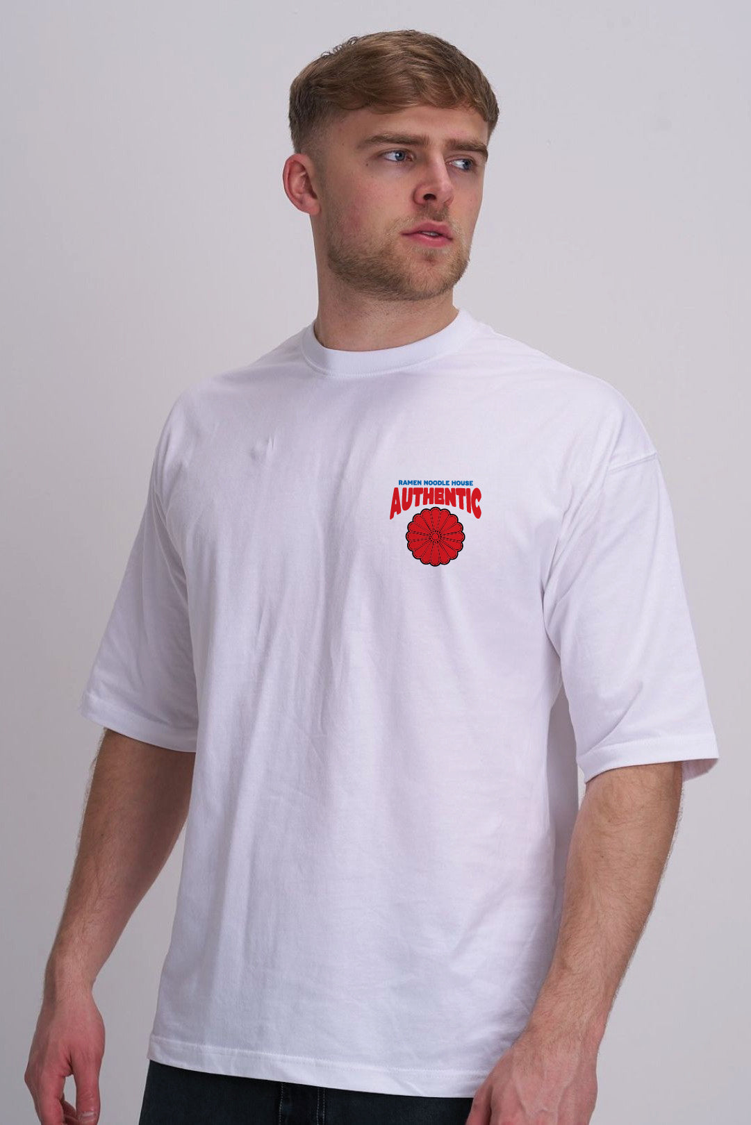 A man wearing a white short-sleeve t-shirt with a red and blue graphic on the left chest that reads 'AUTHENTIC' set against a plain light grey background.
