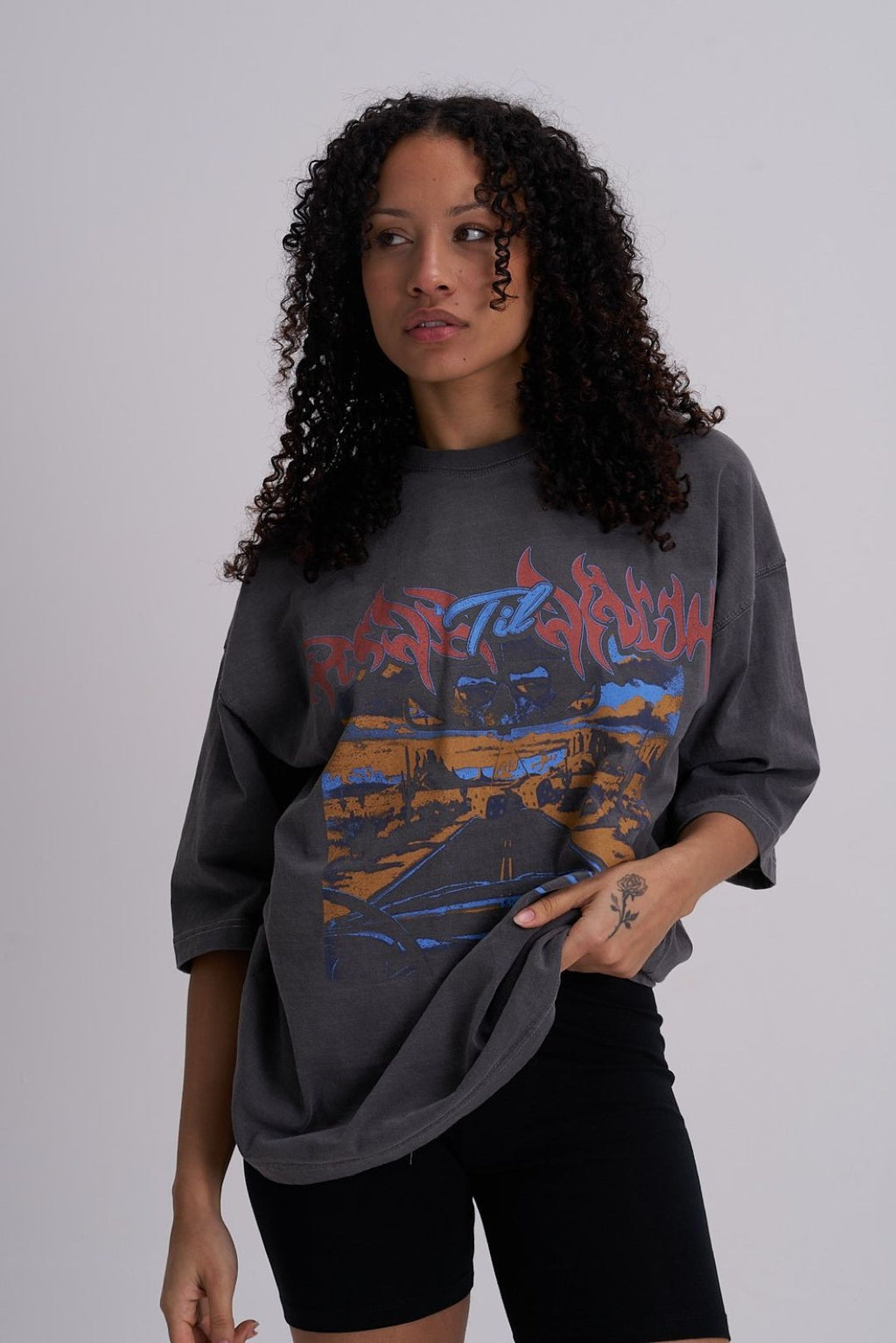 Woman wearing a dark grey oversized t shirt with colourful skull graphic design on a plain background