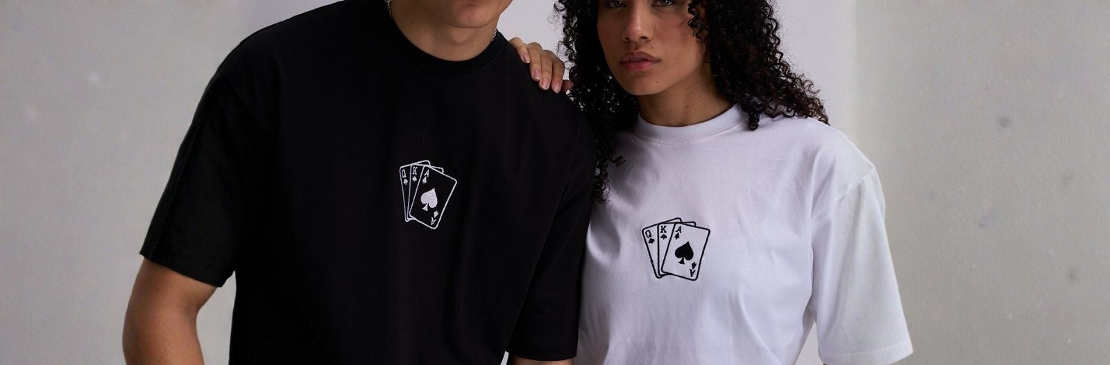 Two people wearing black and white t-shirts with an embroidered deck of cards on a plain background