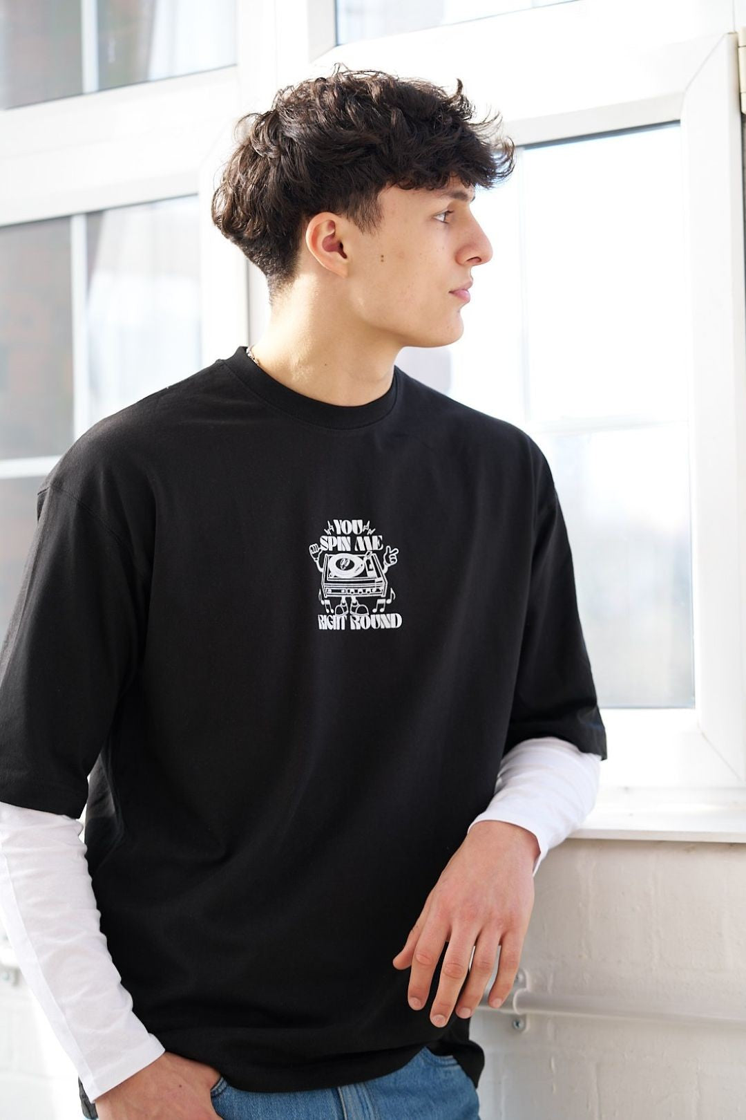 male wearing a black t-shirt with a retro vinyl layer graphic design standing by a window