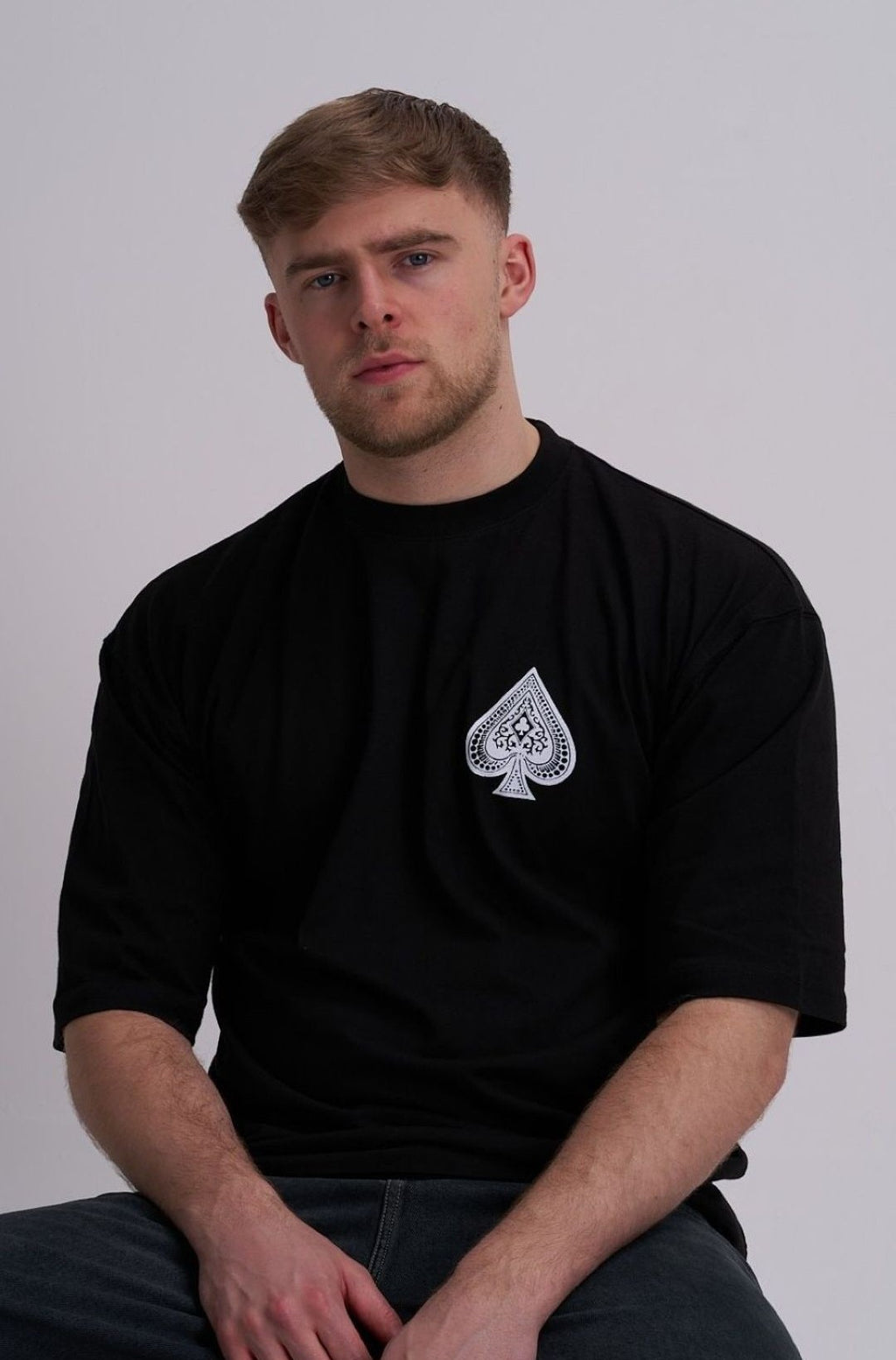 Man wearing a black t-shirt with a white spade logo on a grey background