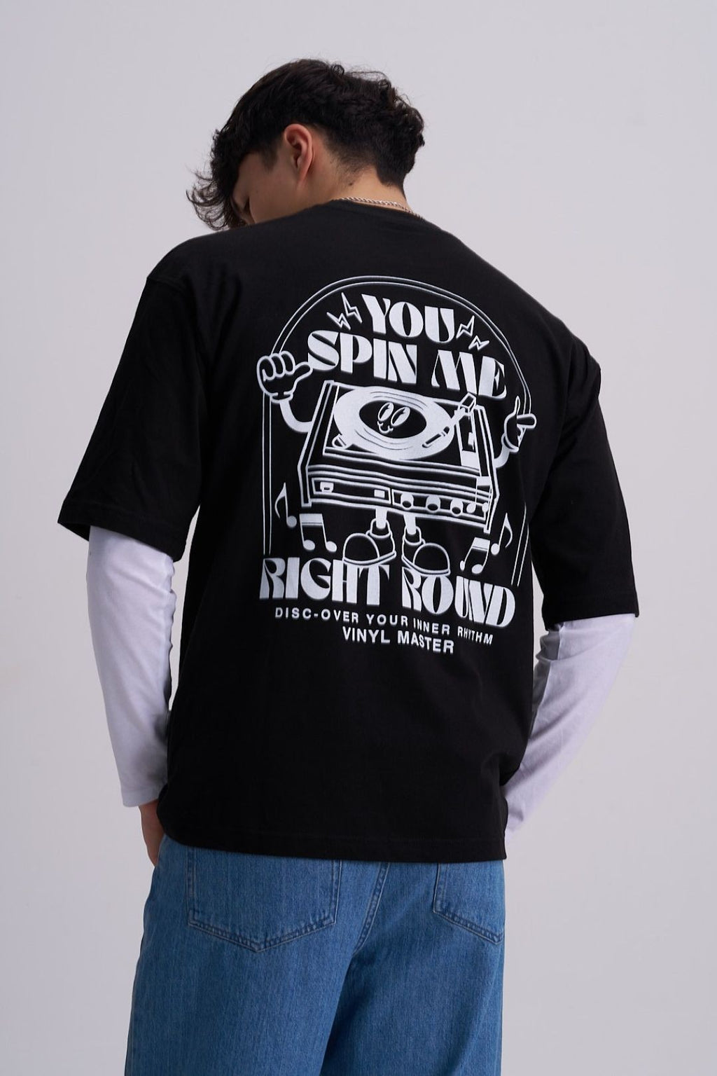 Male wearing a black t-shirt with a retro music vinyl player graphic design on the back, standing against a plain background.
