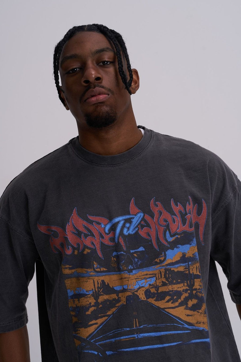 Man wearing a graphic t-shirt with colourful skull and highway design on a plain background