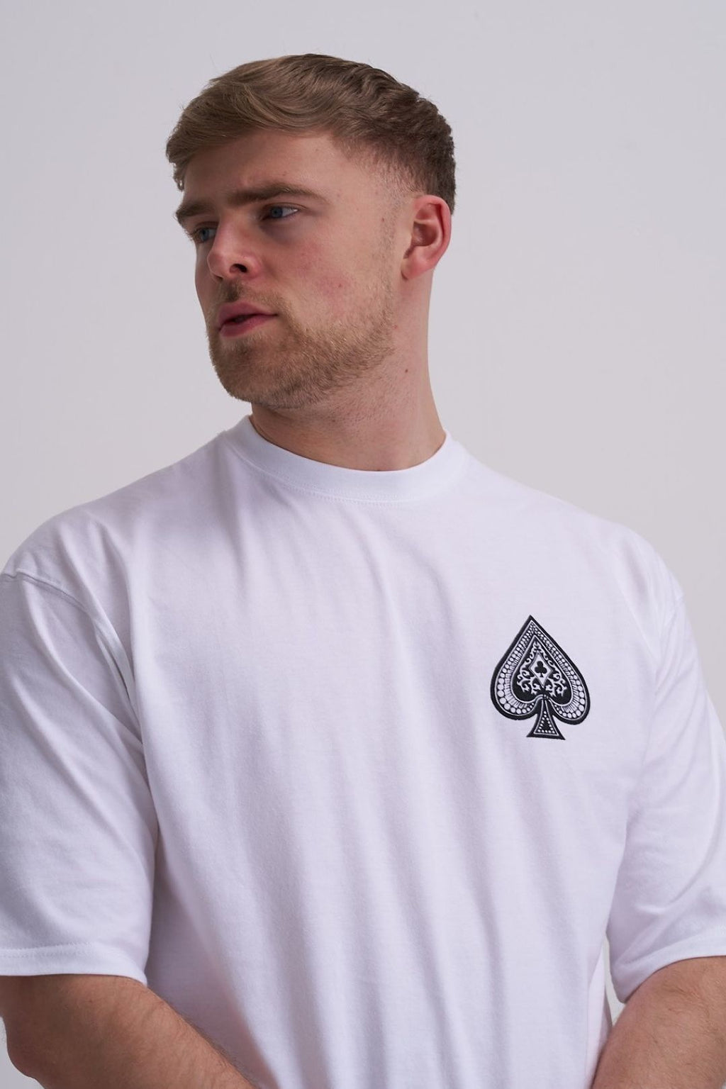 Man wearing a white t-shirt with a black spade symbol on a plain background