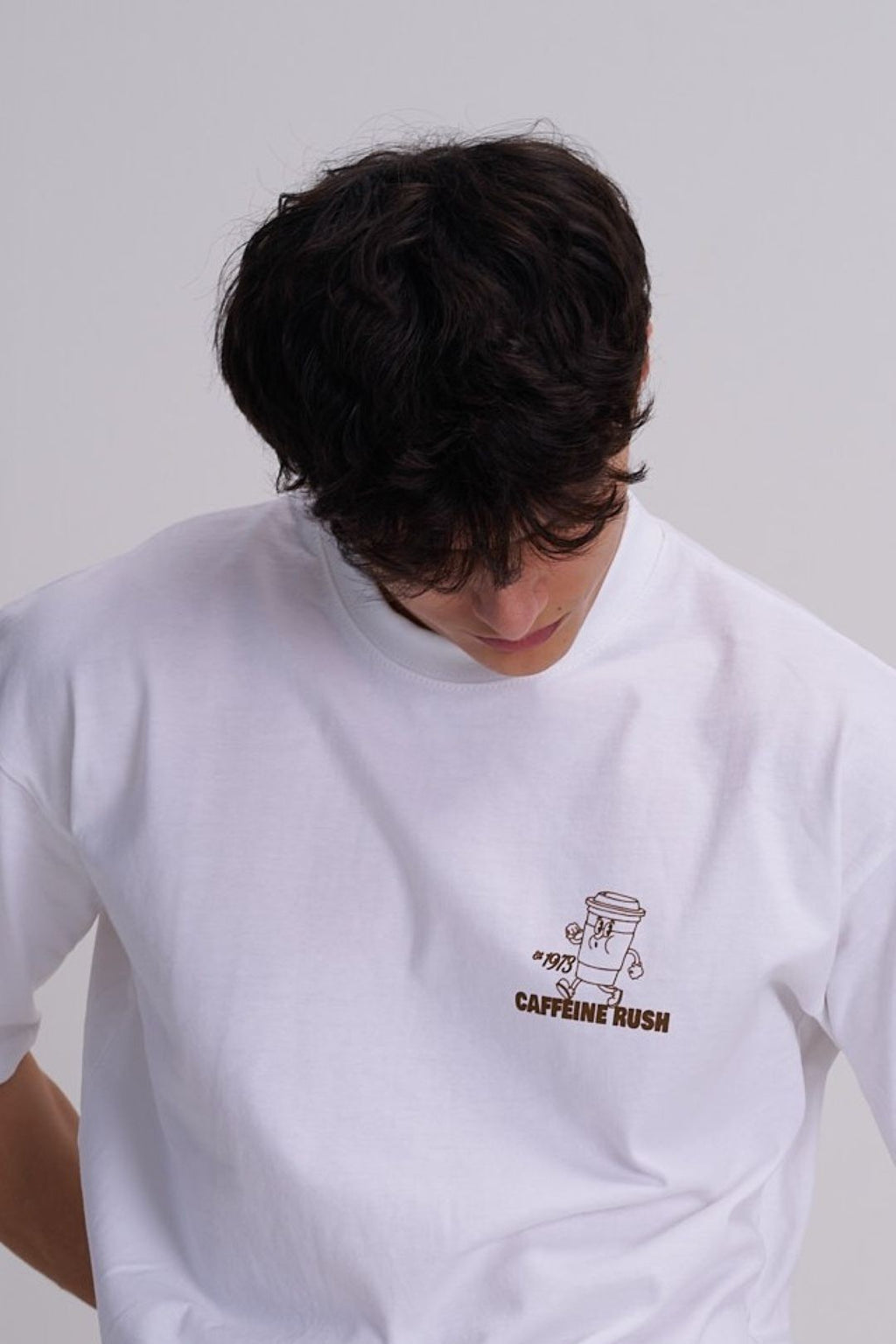 Man wearing a white t-shirt with a  brown takeaway coffee design on a plain background