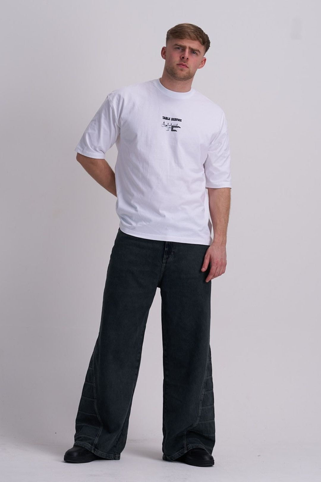 Man wearing a white t-shirt with a chef graphic and black pants on a plain background