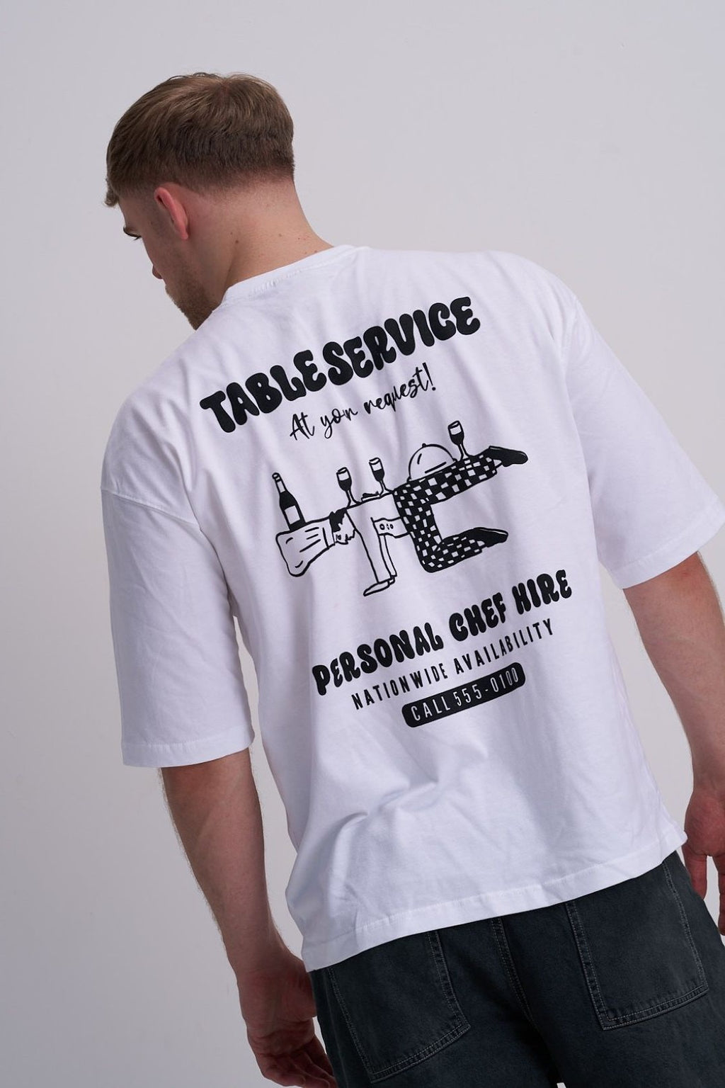 Male wearing a white t-shirt with black text "Table service - personal chef hire and chef graphic on the back.